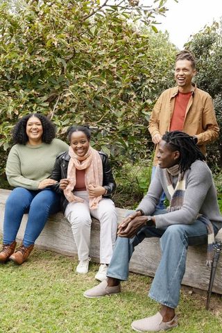 Diverse friends laughing and chatting sitting on wooden log bench in garden
