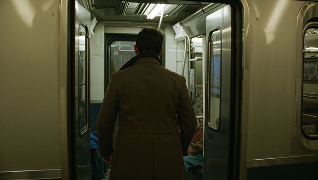 Commuter standing in subway doorway wearing coat and scarf, urban metro interior