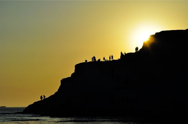 Silhouetted people standing on a cliff during sunset. Ideal for travel blogs, inspirational quotes, adventure advertisements, outdoors activity promotions, and background imagery for websites.