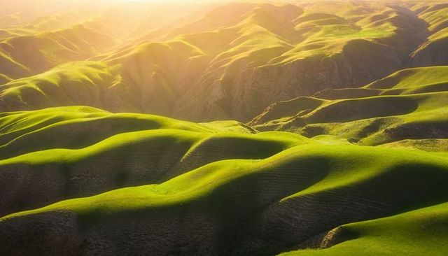 Sunlit rolling emerald ridges golden hour aerial panorama with warm sunbeams and shadows
