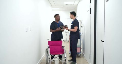 African american and asian healthcare team discussing care near magenta wheelchair hospital corridor