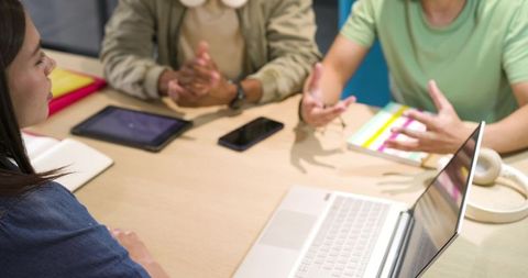 Young professionals collaborating around table with laptop, tablet and headphones