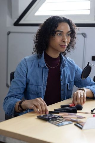 Non-binary creator arranging makeup and recording beauty tutorial under skylight in studio