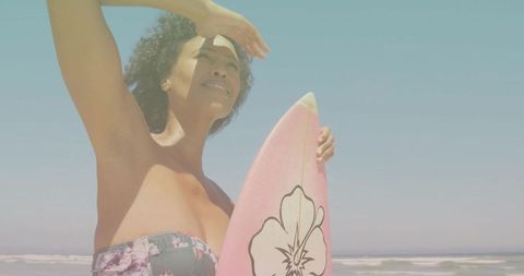 Surfer Shielding Eyes with Pink Hibiscus Surfboard at Beach