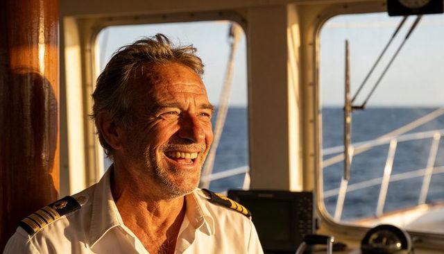 Experienced yacht captain smiling on wheelhouse bridge during golden hour navigation at sea
