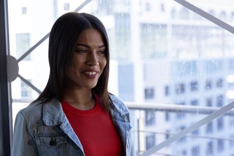 Young woman smiling by rainy window in denim jacket with urban cityscape background