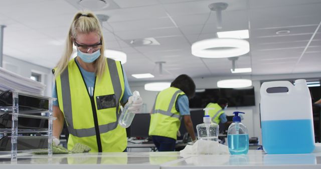 Image showing a professional cleaning crew working in a modern office space. Workers are wearing protective gear, including face masks and high-visibility vests, ensuring workplace hygiene and safety during the pandemic. Useful for illustrating themes such as health safety at work, professional cleaning services, corporate health protocols, and measures taken to prevent illness.