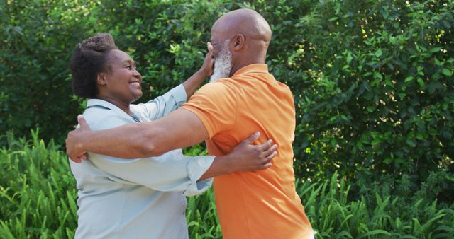 Senior African American couple smiling and dancing together in a lush garden. Perfect for depicting happiness, love in senior years, outdoor activities, and enjoying life in nature.