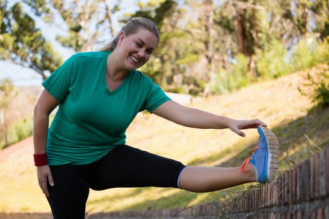 Woman stretching leg on brick wall during outdoor boot camp training. Ideal for promoting fitness, healthy lifestyle, outdoor activities, and wellness programs. Suitable for use in fitness blogs, exercise guides, and health-related advertisements.