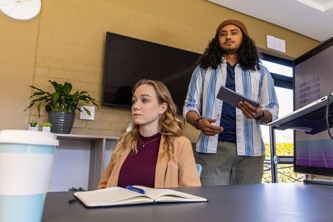 Young professionals collaborating during meeting, woman taking notes, man holding tablet