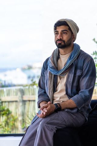 Contemplative man sitting by window gazing toward coast wearing beanie scarf overshirt