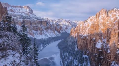 Gliding Aerial Drone Revealing Snowy Canyon with Winding Frozen River and Sunlit Cliffs