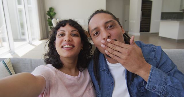 Happy biracial couple sitting on couch taking selfies in living room. wellbeing and domestic lifestyle, relaxing together at home.