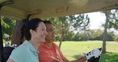 Joyful golfers driving buggy on sunny course