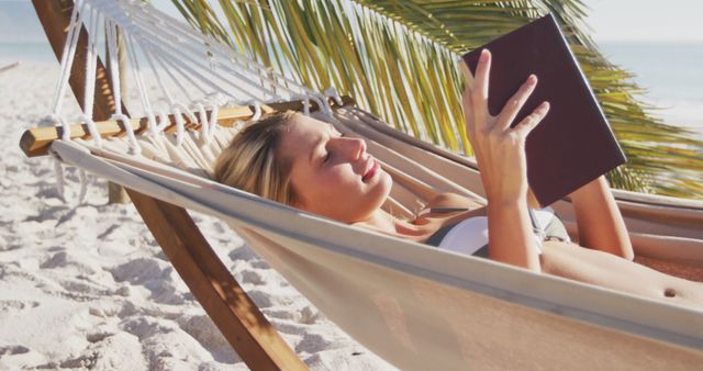 Happy caucasian woman lying in hammock and reading book on beach. Lifestyle, realxation, nature, free time and vacation.