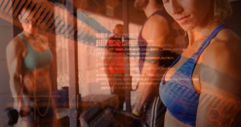 Focusing mid-adult woman lifting dumbbells at gym with mirror reflection and code overlay