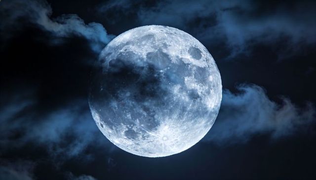 Shining Full Moon Revealing Detailed Craters and Lit Cloud Edges Over Dark Night Sky