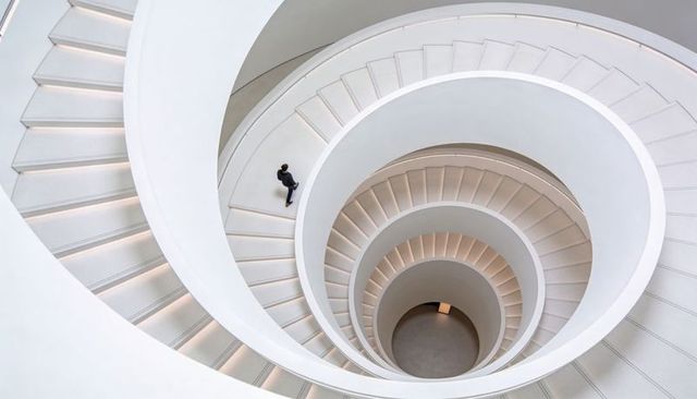Minimalist white spiral staircase with solo figure descending in modern atrium, circular symmetry