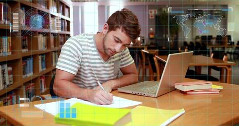 Male student studying and writing notes in library using laptop with futuristic hud overlay