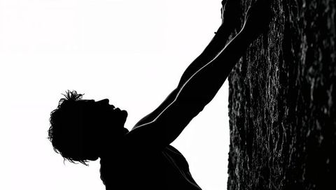 Silhouette climber gripping vertical rock face backlit high-contrast outdoor adventure