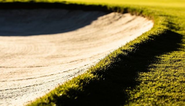 Catching low sunlight on curved sand bunker lip with raked texture and sharp grass edge