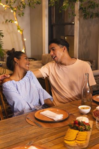 Couple enjoying cozy outdoor dinner on terrace laughing and sharing snacks