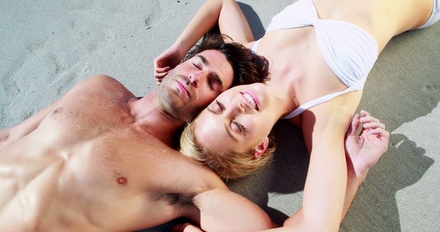 Young couple lying on sandy beach, enjoying sunny weather. Ideal for vacation promotions, travel blogs, romantic getaway advertisements, and lifestyle magazines.