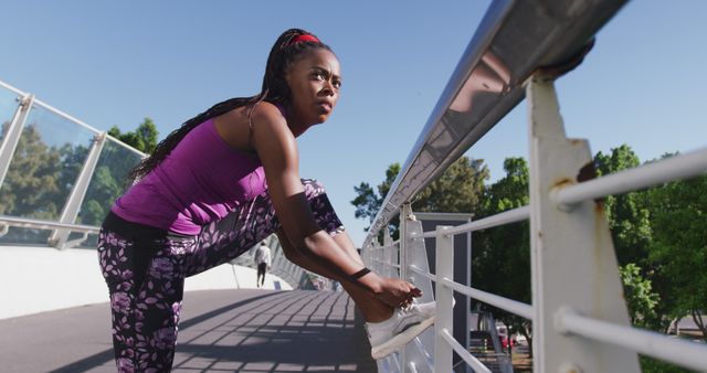 African american woman tying shoe laces on the railing of the city bridge. fitness sports and active lifestyle concept