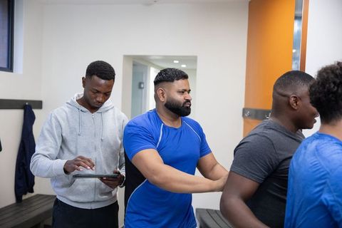 Diverse male athletes preparing in locker room using tablet for pregame strategy teamwork