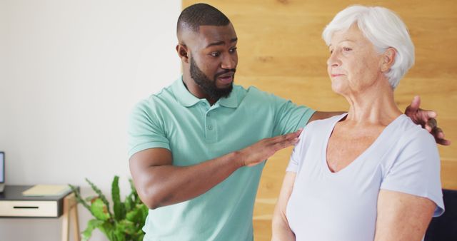 Image of happy african american male physiotherapist exercising with caucasian senior woman. seniors health and nursing home lifestyle concept.