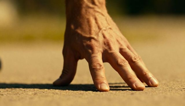 Pressing hand on sunlit pavement close-up showing veins, texture, shadow and grip