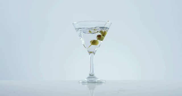 A classic martini with an olive garnish is presented in an elegant glass against a clean, white background, with copy space. Its simplicity and clarity make it an iconic symbol of sophistication in cocktail culture.