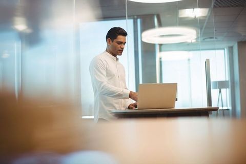 Businessman Using Laptop at High Desk in Modern Office