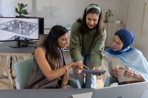 Multicultural women collaborating on tablet reviewing architectural plans in office