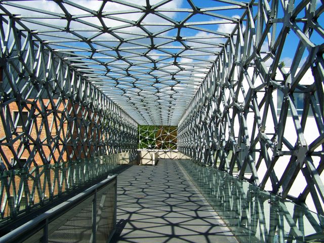 Futuristic metallic walkway with intricate geometric patterns and dramatic shadows across its length. Useful for projects on modern architecture, bridge constructions, and urban design. Perfect for educational materials, architectural brochures, and design inspirations.