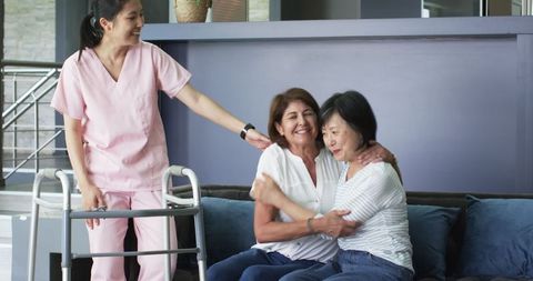 Happy Senior Woman with Nurse and Friend Embracing on Sofa