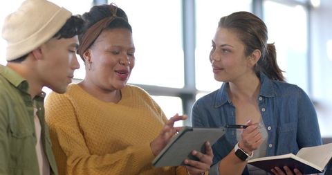 Multiracial team collaborating on tablet and notebook in bright coworking study area