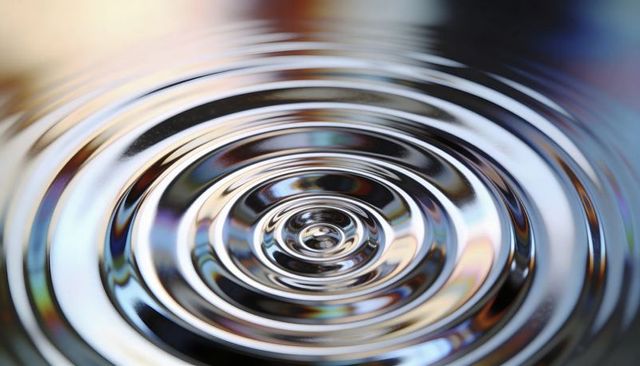 Droplet impacting metallic surface creating concentric ripples with iridescent bokeh