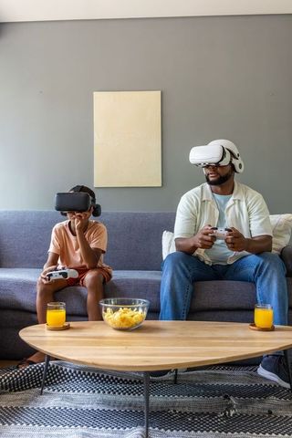 African american father-son gaming on couch with vr headsets and controllers