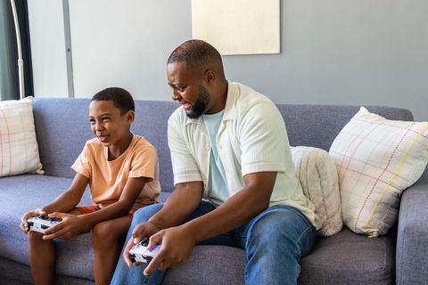 African american father and son playing video game together on couch laughing and bonding