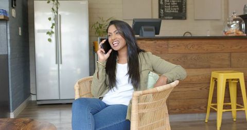Indian woman talking on smartphone while relaxing in modern cafe rattan chair
