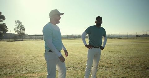 Two baseball teammates standing on sunlit outfield preparing for practice and teamwork