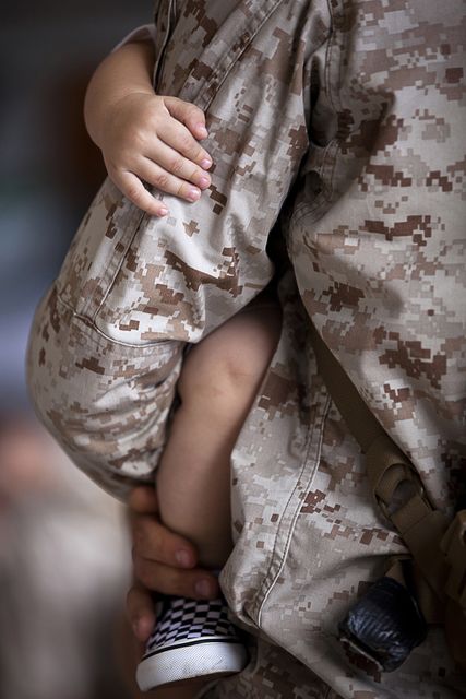 Close-up shows military parent holding child, emphasizing family bonds and parental support in military life. Suitable for discussions on family dynamics, military families, parent-child relationships, and the impact of service on personal life.