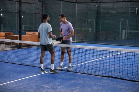 Male players shaking hands over net on indoor blue padel court showing sportsmanship