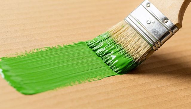 Applying vivid green paint with flat brush on wooden board closeup bristles texture