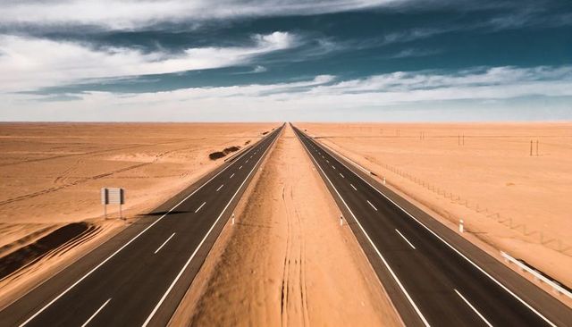 Stretching divided highway running through arid desert plain under dramatic teal sky