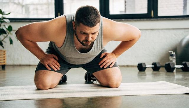 Determined man kneeling on mat leaning forward during home gym strength training session