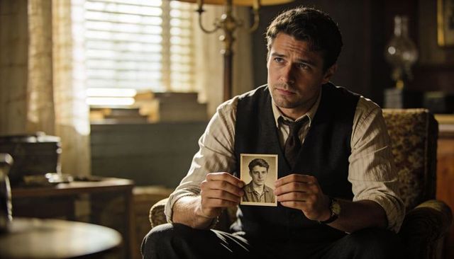 Brooding investigator holding vintage portrait in wood-panel study, moody lamplight