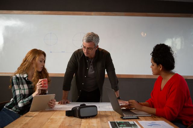 Front view of a Caucasian man, a Caucasian woman and a biracial woman working in a creative office, brainstorming in a conference room, with a whiteboard in the background