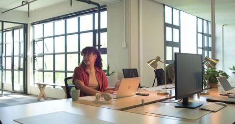 Working woman using laptop in modern open-plan office with daylight and greenery